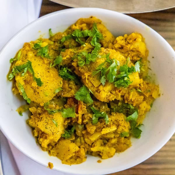 A white bowl filled with Rasoi's Indian aloo gobi, garnished with fresh cilantro.