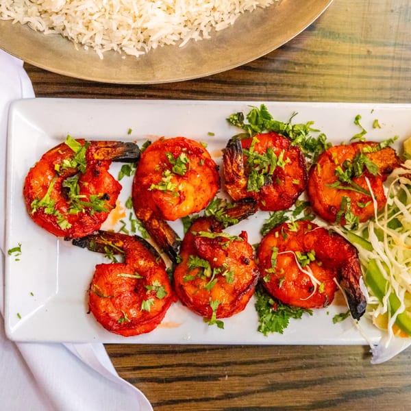 Rasoi's Tandoori Shrimp, six vibrant red shrimp garnished with cilantro, served with rice and salad.
