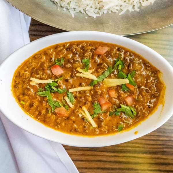 A white bowl of Rasoi's Indian dal makhani, garnished with cilantro, ginger, and tomatoes.