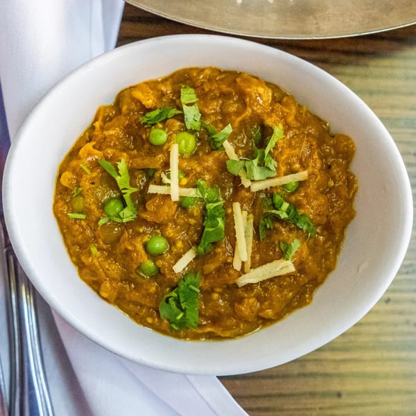 A white bowl of Rasoi's Indian curry, garnished with green peas, cilantro, and ginger.