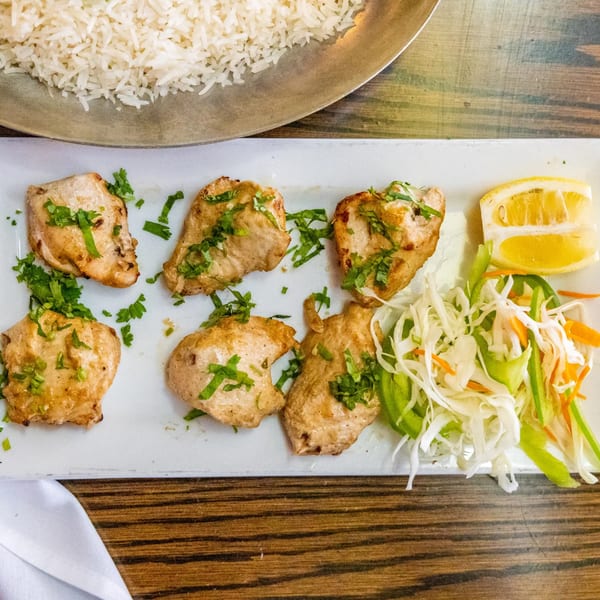 Six pieces of Indian chicken tikka with cilantro, a lemon wedge, and shredded salad.
