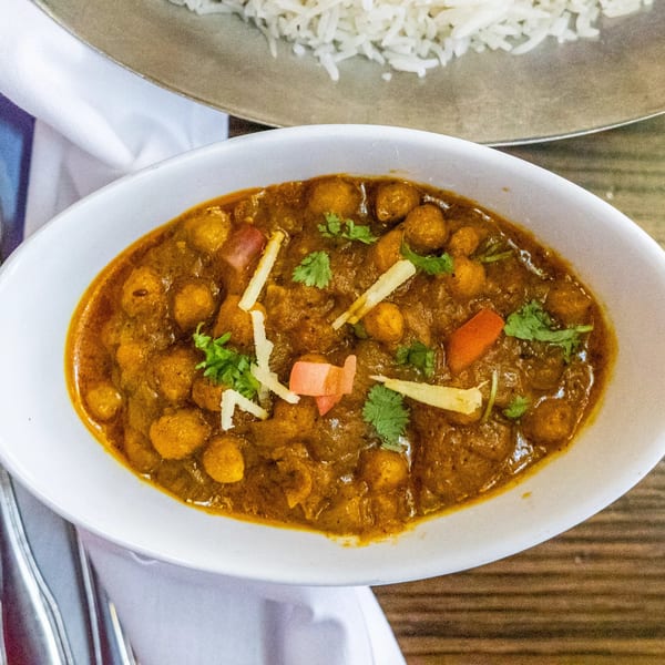 A white bowl of Rasoi's chana masala with cilantro and ginger, next to rice.