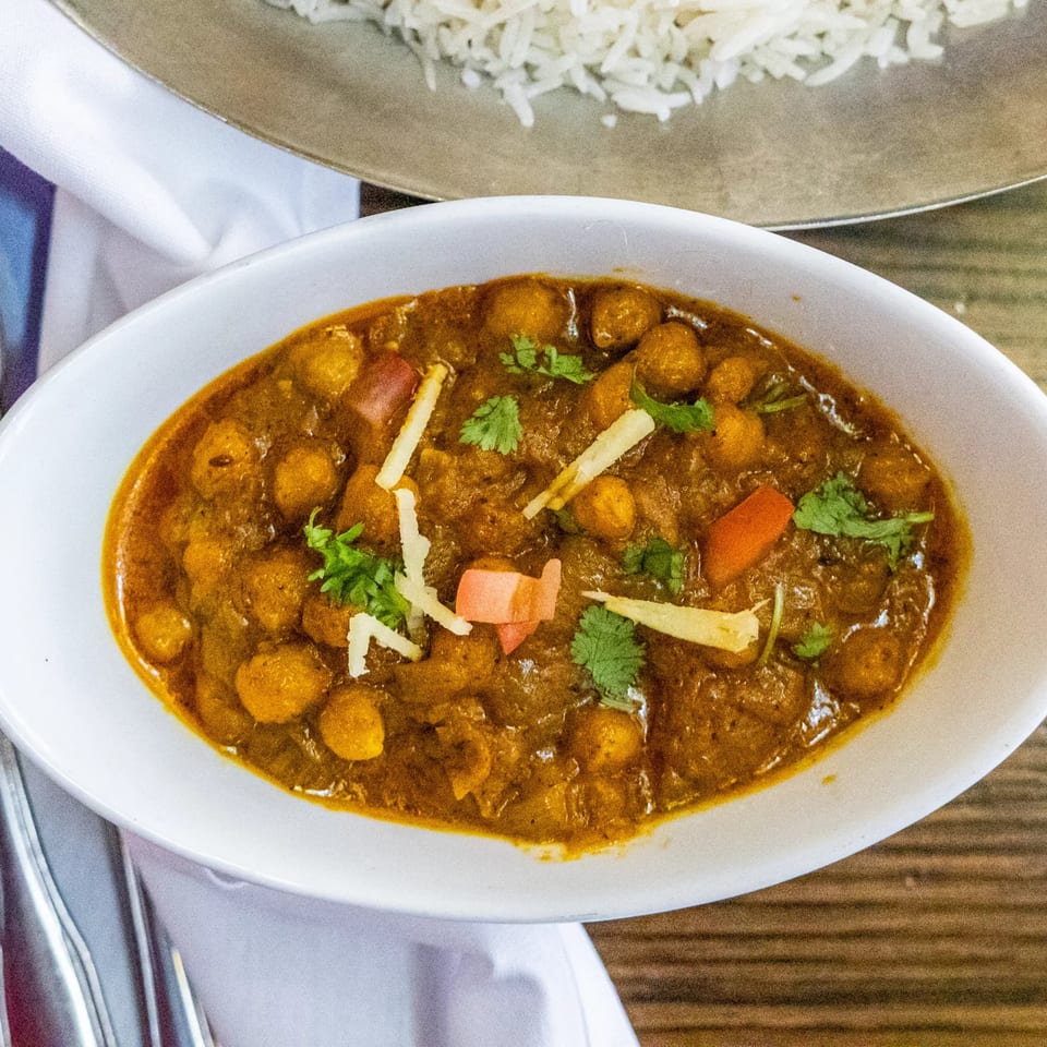 A white bowl of Rasoi's chana masala with cilantro and ginger, next to rice.
