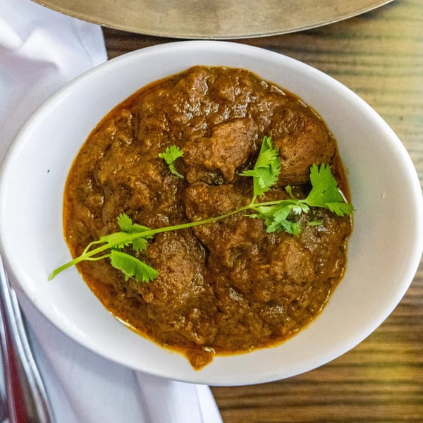 Rasoi's Indian curry with meat pieces and fresh cilantro in a white bowl.