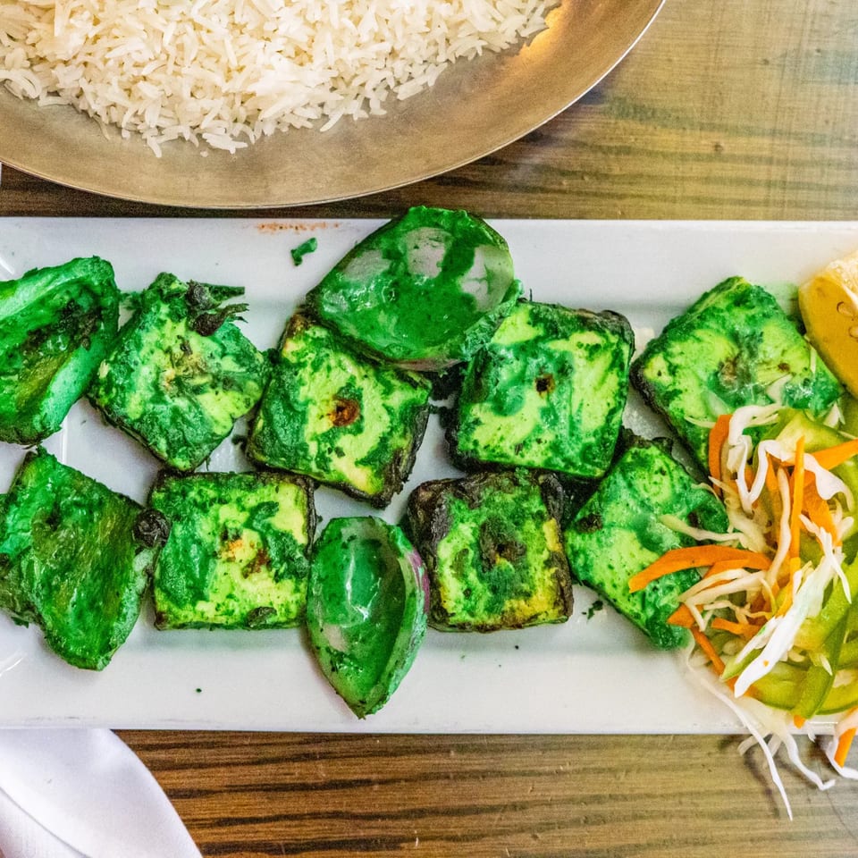 Green paneer tikka and vegetables on a white plate with rice in the background at Rasoi.