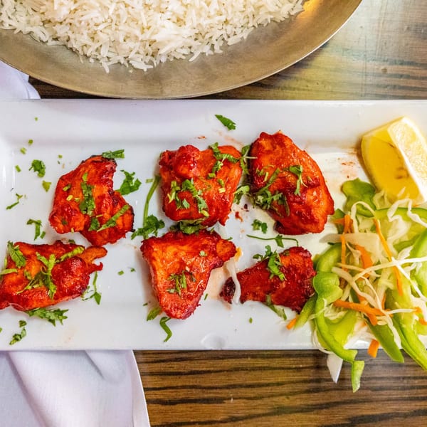 Rasoi's chicken tikka with cilantro, lemon, and a side salad, with rice in the background.